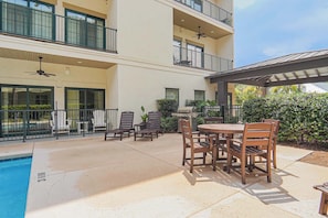 A poolside area with outdoor seating and a barbecue grill. - Gated King Condo Steps to Pier Village (St. Simons Island)