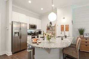 A modern kitchen with a central island, stainless steel appliances, and a hanging light fixture. - Gated King Condo Steps to Pier Village (St. Simons Island)