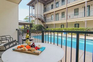 A balcony with a pool, a table with a cheese board, and a bottle of wine. - Gated King Condo Steps to Pier Village (St. Simons Island)