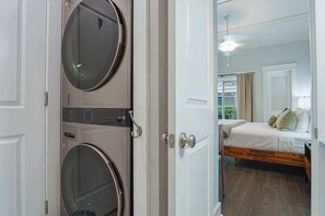 A room with a bed, a window with curtains, and a door with a circular mirror. - Gated King Condo Steps to Pier Village (St. Simons Island)