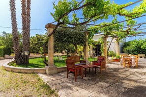 Eine Außenpatio-Terrasse mit Steinboden, Holzmöbeln und einer Pergola mit Weinreben.