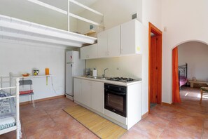 Eine kompakte Küche mit Gasherd, Backofen und weißen Schränken. Ein kleiner Essbereich mit einem Stuhl und einem Tisch ist ebenfalls vorhanden.