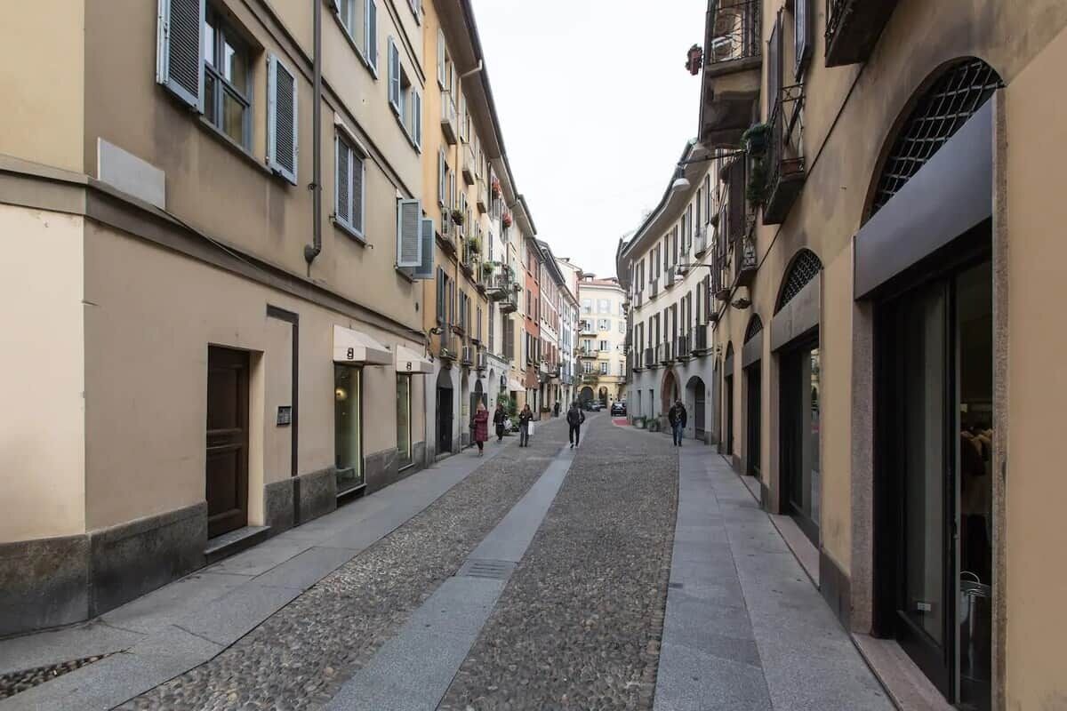 A narrow street lined with buildings, some with balconies and awnings.