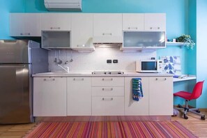 Une cuisine compacte avec des meubles blancs, un réfrigérateur en acier inoxydable, un four à micro-ondes et une chaise de bureau rouge.