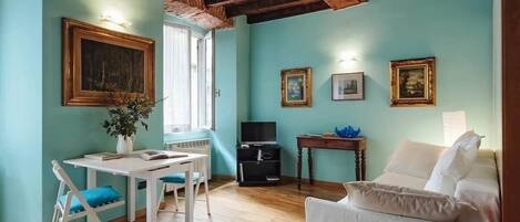 Een woonkamer met houten plafond, een witte bank, een tafel met stoelen en een tv-meubel.