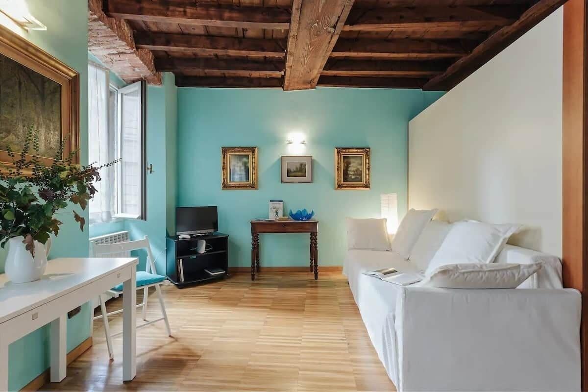 A living room with a white sofa, a small table, a TV, and a painting on the wall.