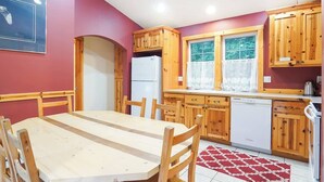 Eine Küche mit Holzausstattung, einem weißen Kühlschrank, einem Geschirrspüler und einem Esstisch mit Stühlen.