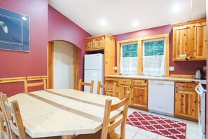 A kitchen with wooden cabinets, a white refrigerator, a dishwasher, and a dining table with chairs. - Creekside Cabin • Hot Tub, Pool & Ping Pong (Deming)