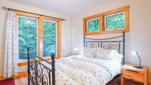 Ein Schlafzimmer mit einem Bett, zwei Fenstern, einem Nachttisch und einem roten Teppich.