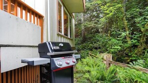 Ein tragbarer Grill auf einer Holzterrasse, im Hintergrund ein Haus.