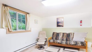 Ein Zimmer mit einer Couch, einem Sessel, einem Fenster mit Vorhängen, einem gerahmten Bild und einem Feuerlöscher.
