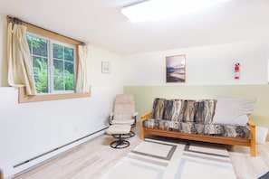 A room with a sofa, a chair, a window with curtains, a framed picture, and a fire extinguisher. - Creekside Cabin • Hot Tub, Pool & Ping Pong (Deming)