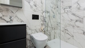 Een badkamer met een wit toilet, een douche en een marmeren wand.