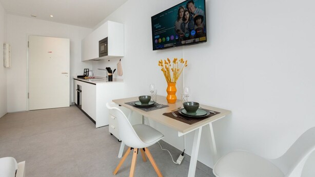 Een moderne keuken met witte kasten, een flatscreen televisie boven de aanrechten en een eethoek met een tafel gedekt voor twee personen.
