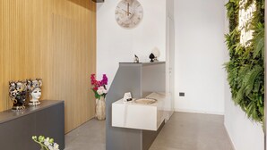 A modern reception area with a wooden panel wall, a marble clock, a reception desk, and a green plant wall. - Deluxe Suite with Balcony, Wi-Fi, and Air Conditioning (Partinico)