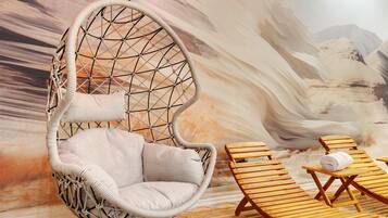 A hanging chair in a room with a desert mural, wooden lounge chairs, and a woven rug.