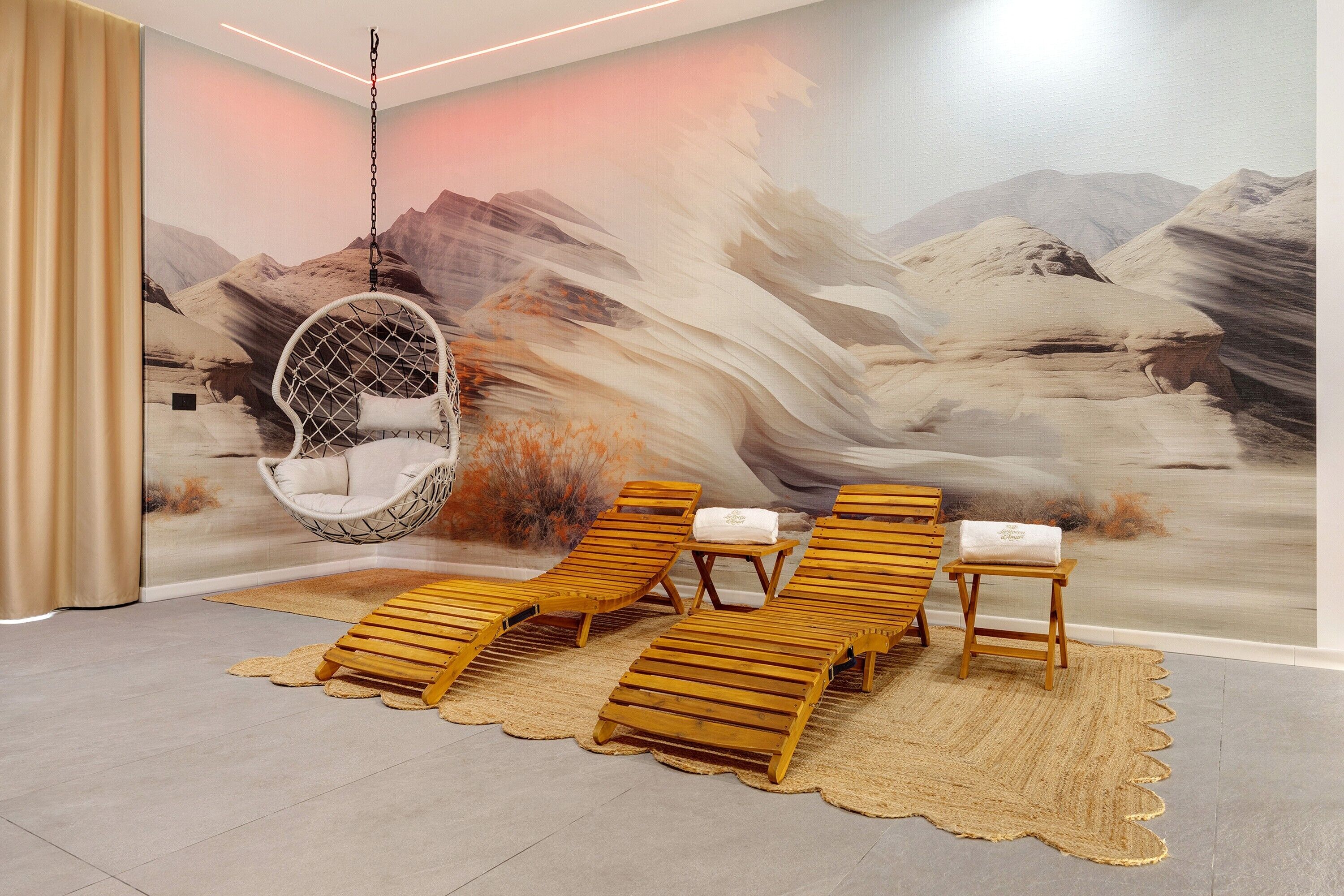 A room with a hanging chair, lounge chairs, and a mural of a mountainous landscape.