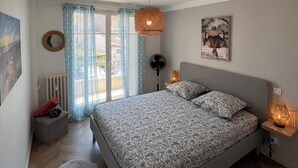 Ein Schlafzimmer mit Bett, Standventilator, Heizung, Teppich und einem Fenster mit Vorhängen.