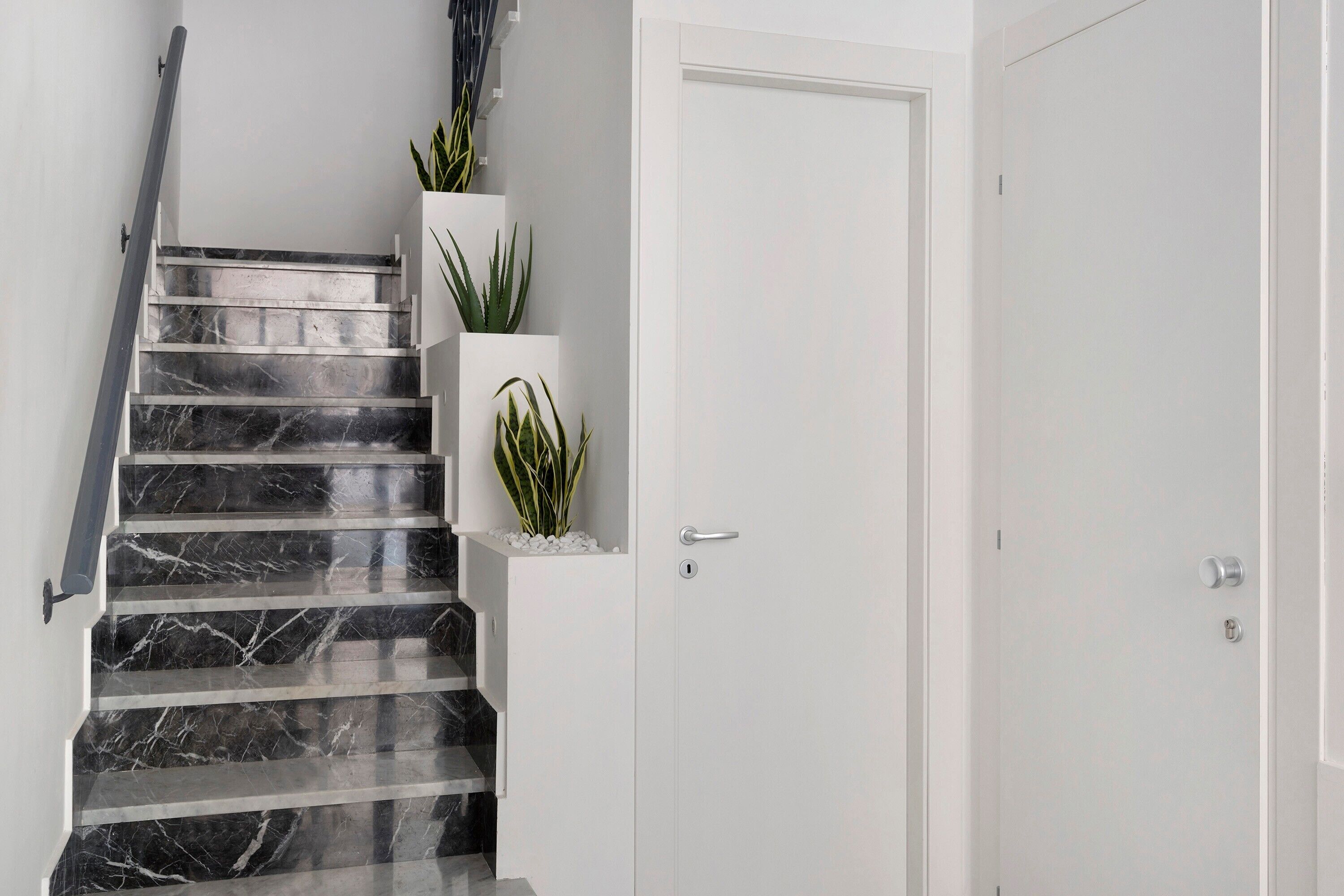 A staircase with black marble steps, white walls, and a white door with a silver handle.