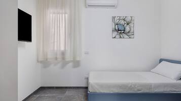 A bedroom with a bed, a window with sheer curtains, an air conditioning unit, and a wall-mounted artwork.