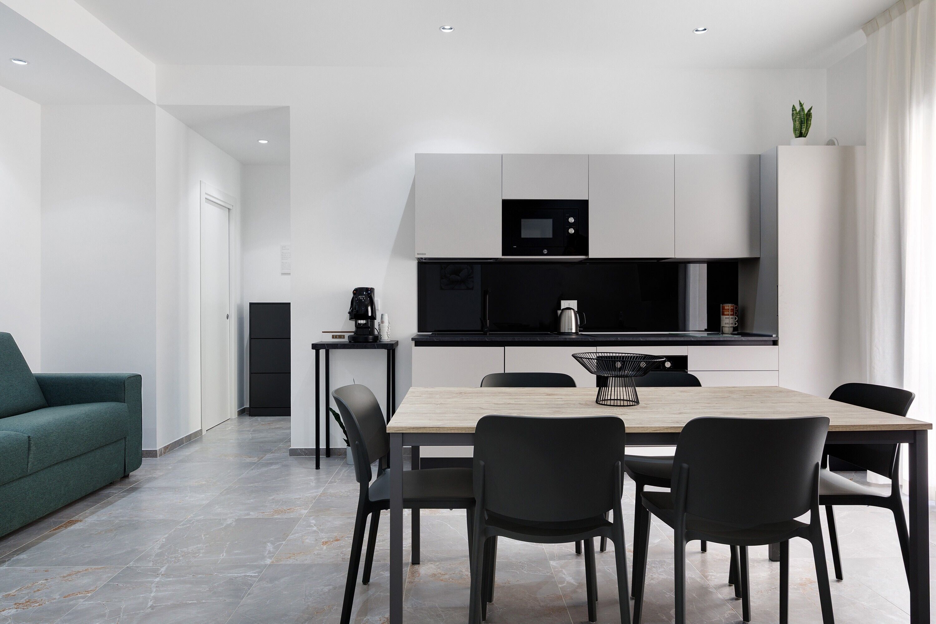 A modern kitchen with a dining area, a sofa, and a coffee machine.