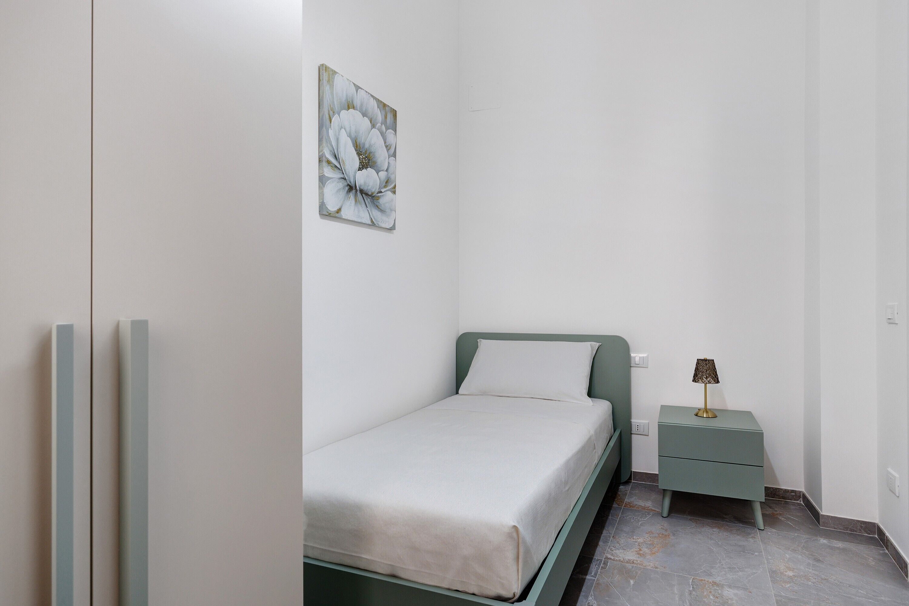 A bedroom with a bed, a nightstand, a wall-mounted artwork, and a wardrobe.