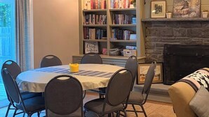 Uma sala de jantar com uma mesa redonda, seis cadeiras, uma estante de livros e uma lareira.