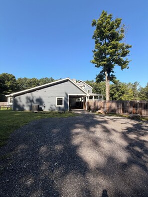 A two-story building with a covered porch, a fenced yard, and a large tree.