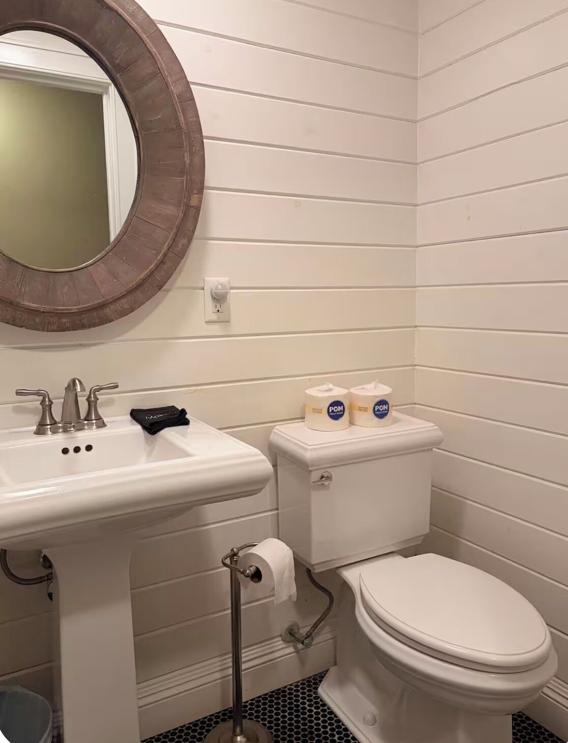 Une salle de bain avec un lavabo blanc, des toilettes et un miroir rond.