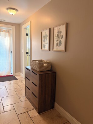 A hallway with a wooden cabinet, a basket on top, and two framed botanical prints on the wall.
