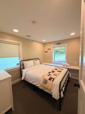 A bedroom with a bed, a window, a bedside table, and a door.