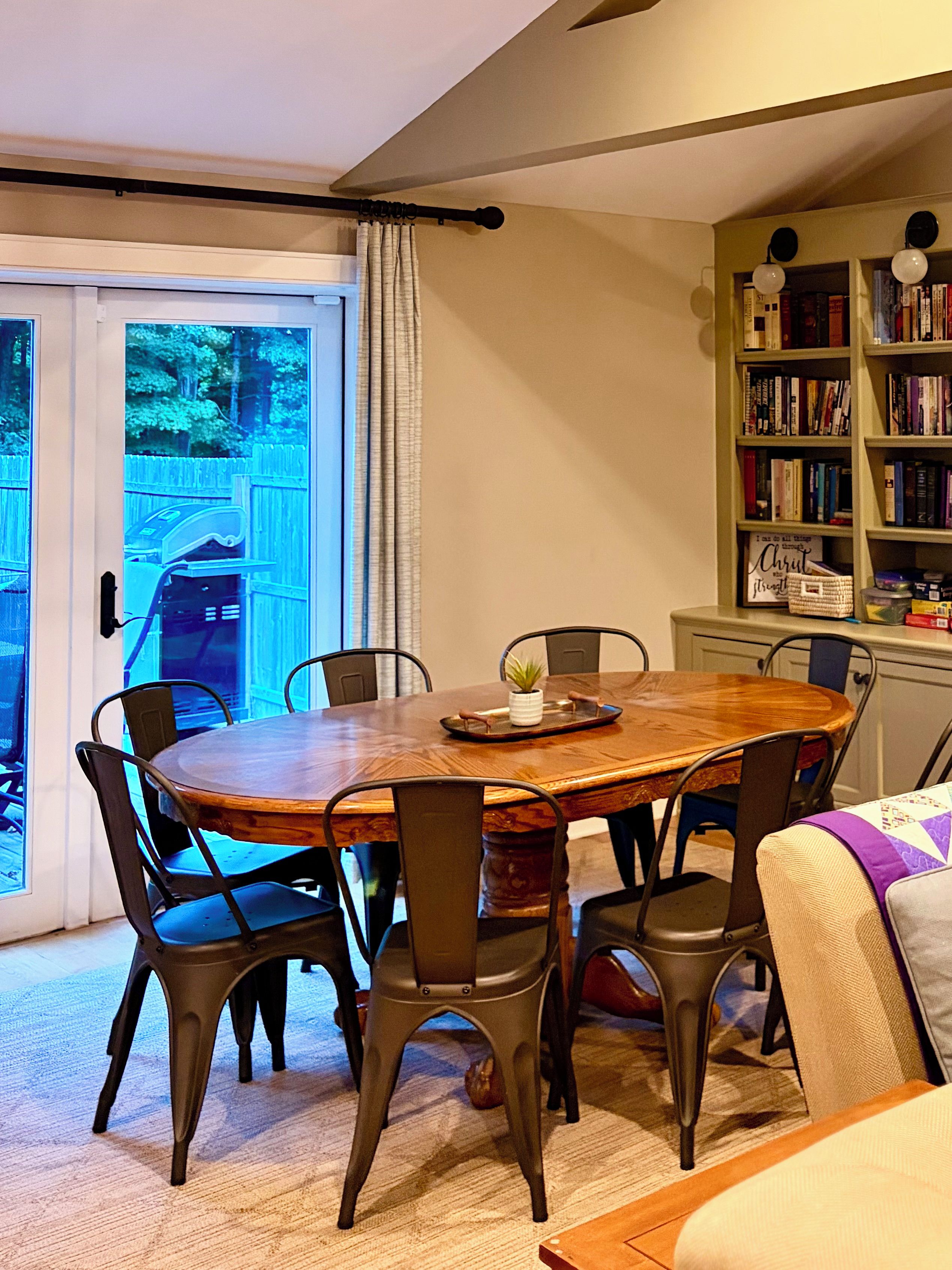 Un coin repas avec une table en bois entourée de chaises, une bibliothèque et une vue à travers une porte vitrée.