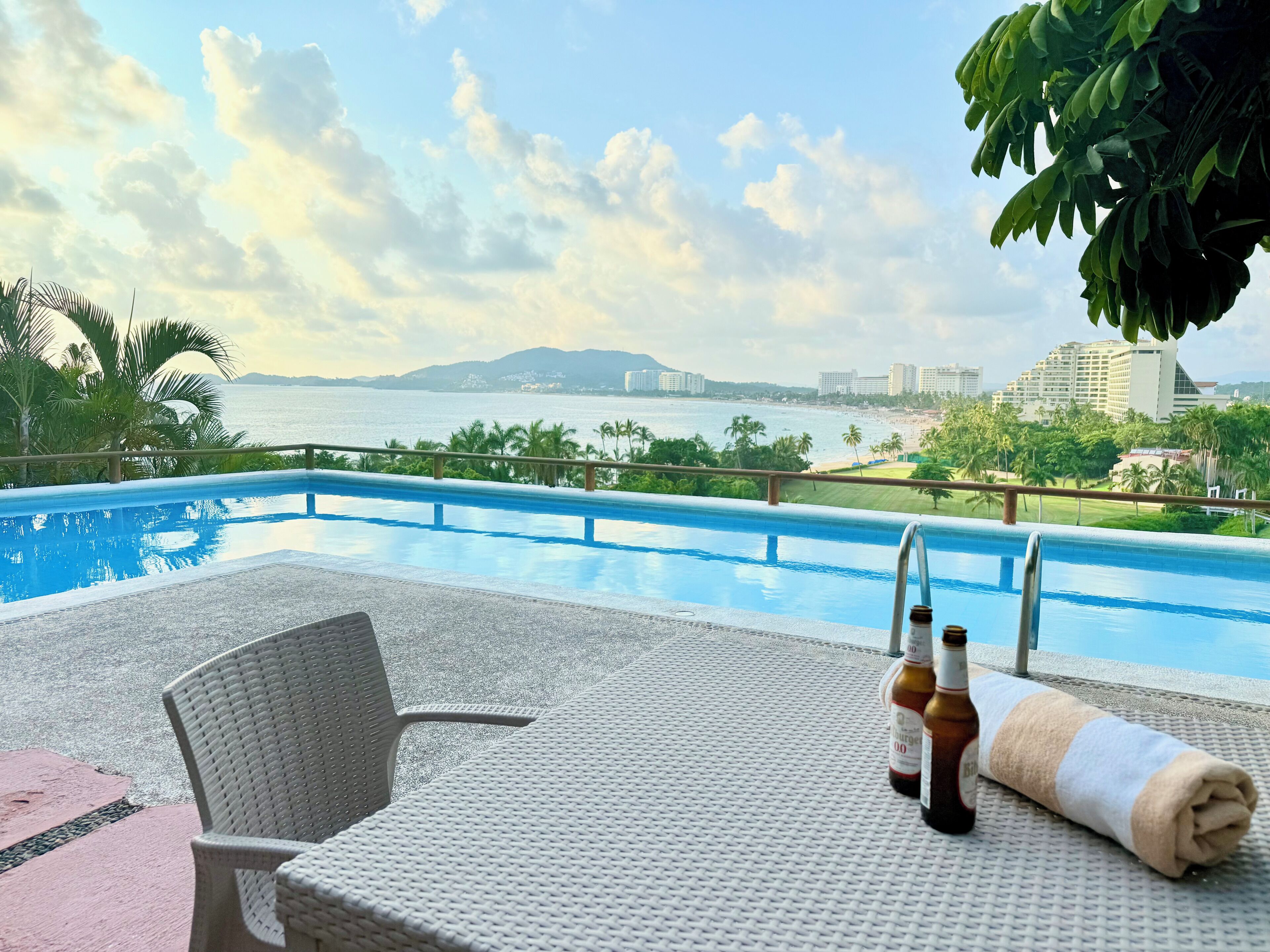 A poolside area with a view of the sea, a chair, and a towel.