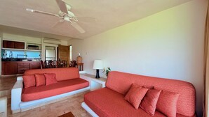 A living room with two red sofas, a wooden coffee table, and a ceiling fan. - Vista Pacífico • Beachfront Condo • Pool • Ixtapa-Zihuatanejo (Ixtapa Zihuatanejo)