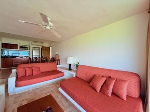 A living room with two red sofas, a wooden coffee table, and a ceiling fan. - Vista Pacífico • Beachfront Condo • Pool • Ixtapa-Zihuatanejo (Ixtapa Zihuatanejo)