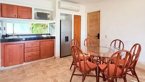 A kitchen with wooden cabinets, a stainless steel refrigerator, and a glass dining table surrounded by wicker chairs. - Vista Pacífico • Beachfront Condo • Pool • Ixtapa-Zihuatanejo (Ixtapa Zihuatanejo)