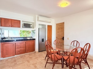 A kitchen with wooden cabinets, a stainless steel refrigerator, and a glass dining table surrounded by wicker chairs. - Vista Pacífico • Beachfront Condo • Pool • Ixtapa-Zihuatanejo (Ixtapa Zihuatanejo)
