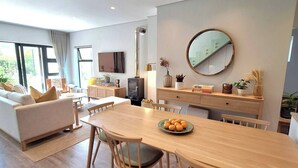 A modern living room with a sofa, dining table, and chairs. There is a television, a fireplace, and a large mirror on the wall. - Rustling Reeds Sanctuary (Cape Town)