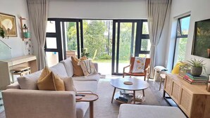 A modern living room with a sofa, armchairs, a coffee table, and a TV. - Rustling Reeds Sanctuary (Cape Town)