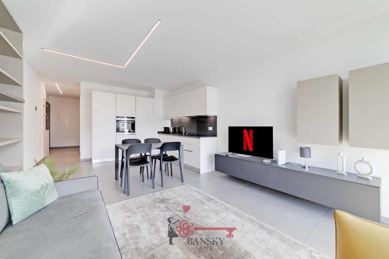 Ein modernes Wohnzimmer mit einer Couch, einem Couchtisch, einem Fernseher und einem Essbereich mit Stühlen.