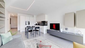 Ein modernes Wohnzimmer mit einer Couch, einem Couchtisch, einem Fernseher und einem Essbereich mit Stühlen.