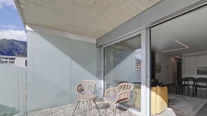 Un intérieur moderne avec une porte vitrée donnant sur un balcon, des fauteuils en osier et un coin repas comprenant une table et des chaises.