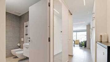 Ein modernes Badezimmer mit Toilette, Handtuchhalter und einer Glastür, die in einen Wohnbereich mit Sofa und Couchtisch führt.