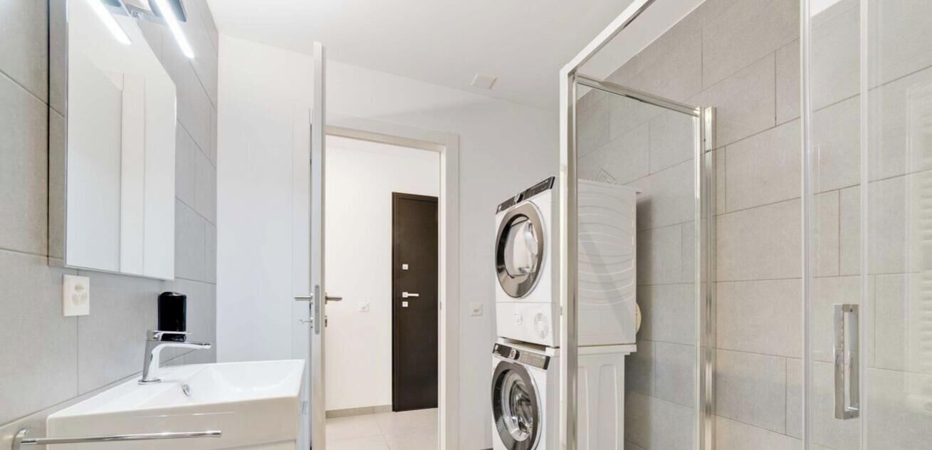 Ein modernes Badezimmer mit Waschbecken, Spiegel und gestapelten Waschmaschinen.