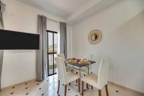Ein Essbereich mit einem Tisch für vier Personen, einem an der Wand montierten Fernseher und einem Balkon mit Blick.