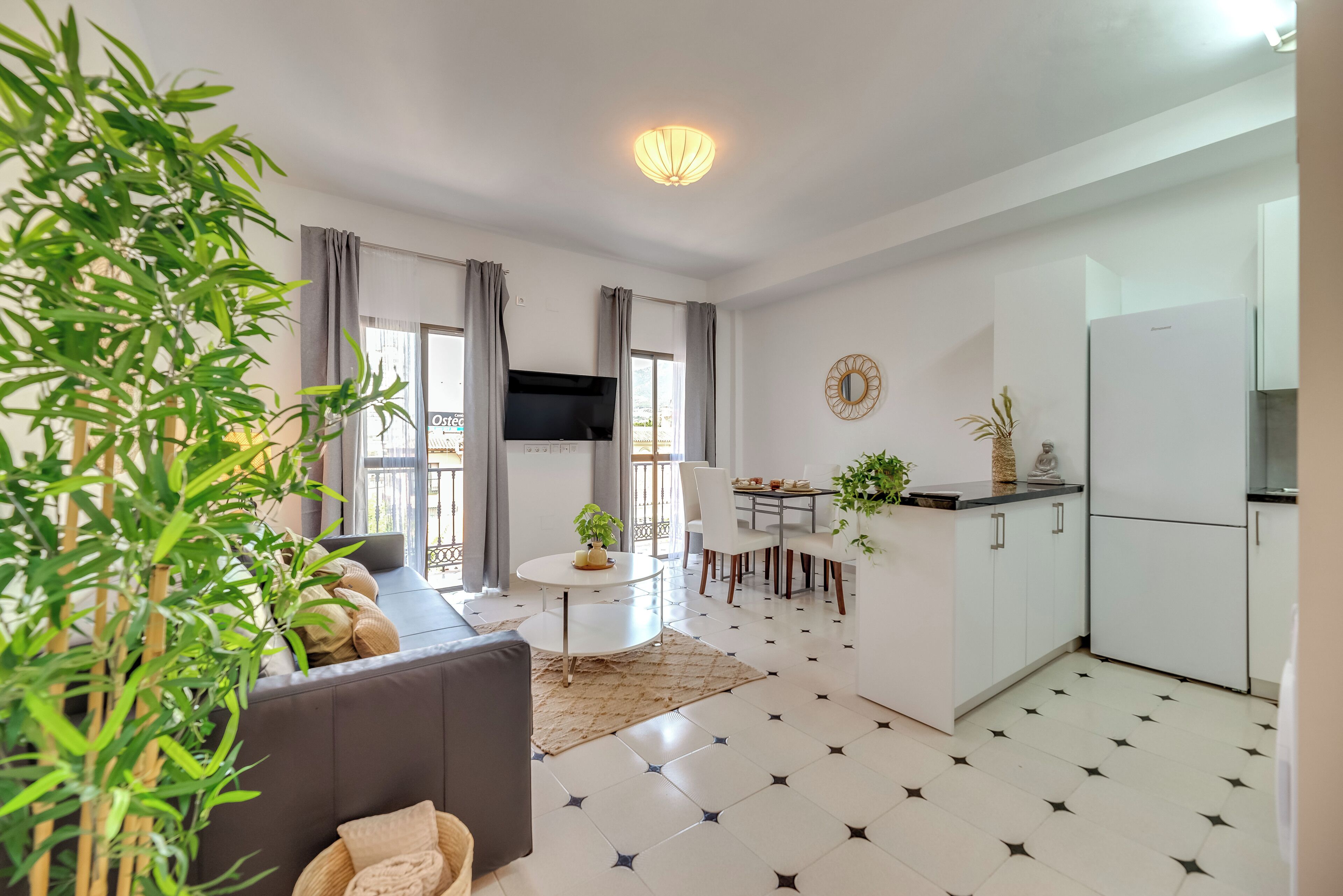 A modern living room with a sofa, a dining table, and a kitchen area with a refrigerator.