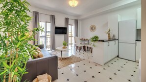 Ein modernes Wohnzimmer mit Sofa, Esstisch und Küchenbereich inklusive Kühlschrank.