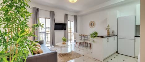 A modern living room with a sofa, a dining table, and a kitchen area with a refrigerator.