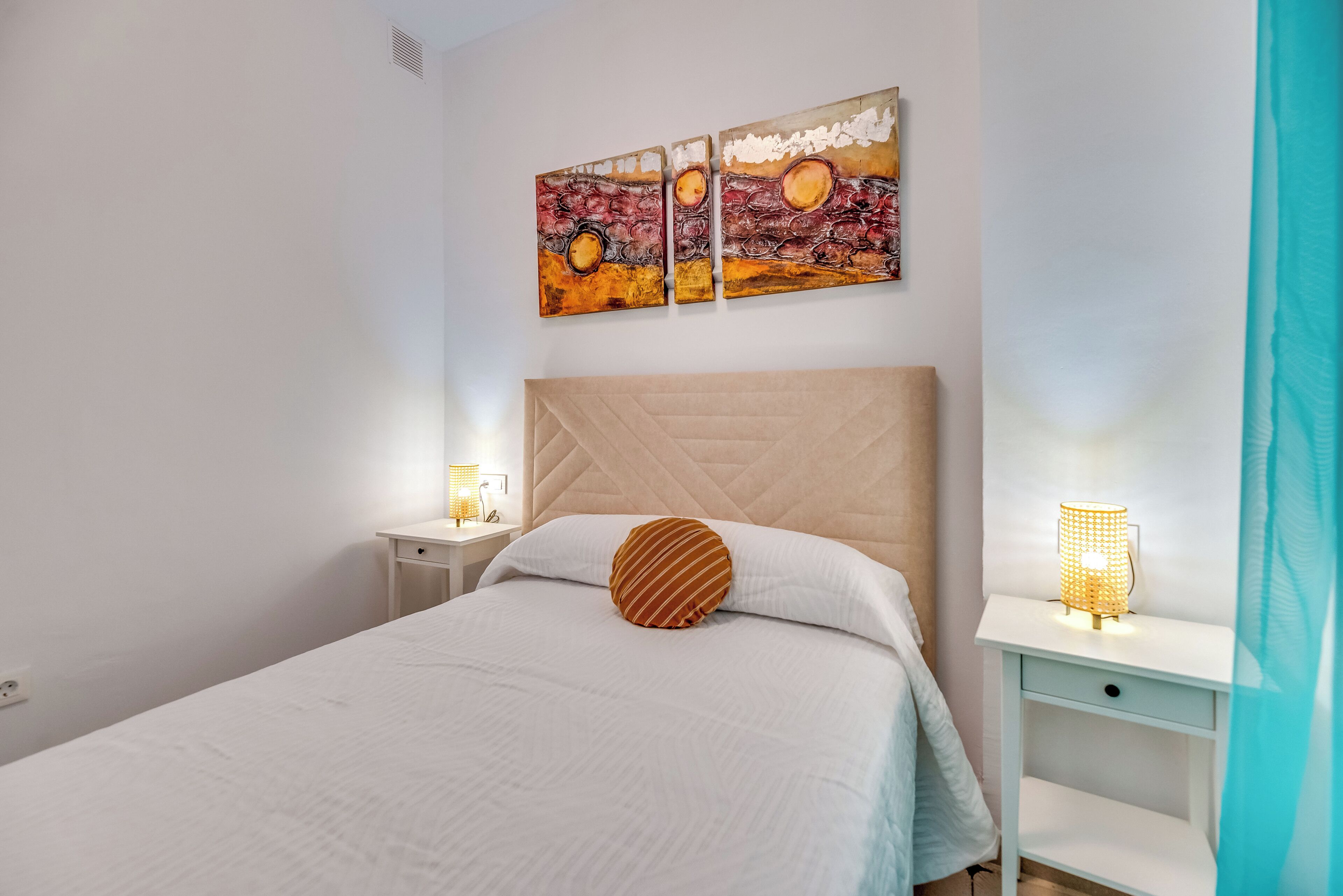 A bedroom with a bed, a nightstand, a bedside lamp, and a wall-mounted artwork.