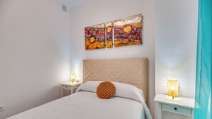 Ein Schlafzimmer mit einem Bett, einem Nachttisch, einer Nachttischlampe und einem an der Wand befestigten Kunstwerk.